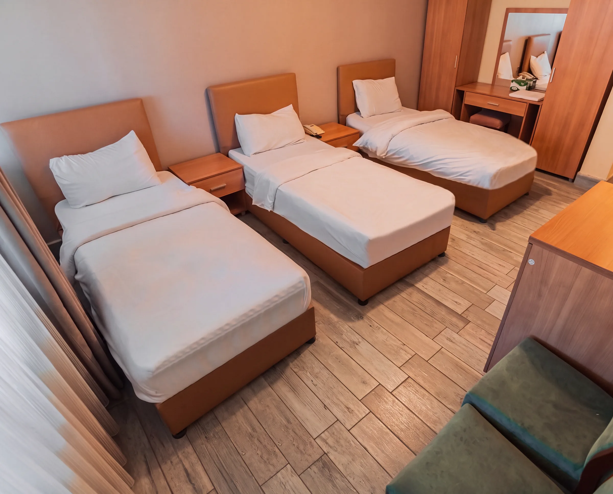A hotel room with three single beds, bedside tables and a wardrobe and dressing table with mirror