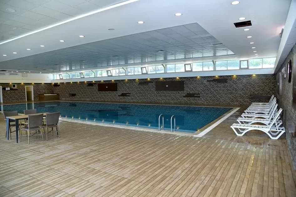 Indoor swimming pool with poolside tables and white loungers.