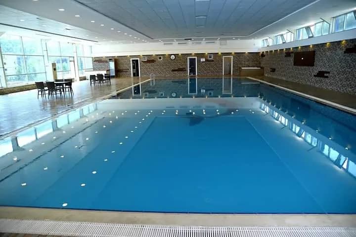 Indoor swimming pool with a tiled wall and tall windows along the side.