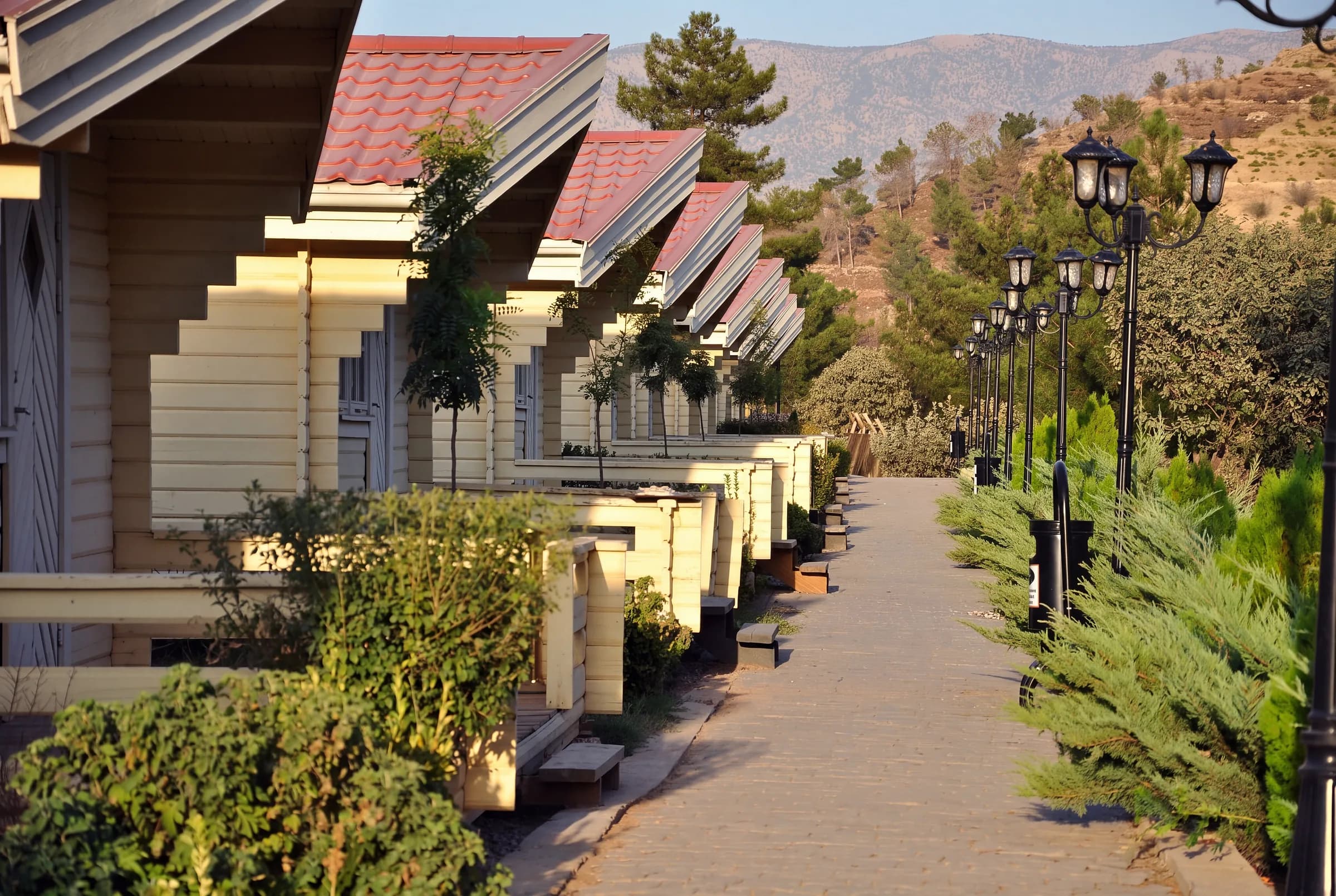A row of wooden cabins beside garden lamps, with Safeen in the distance.