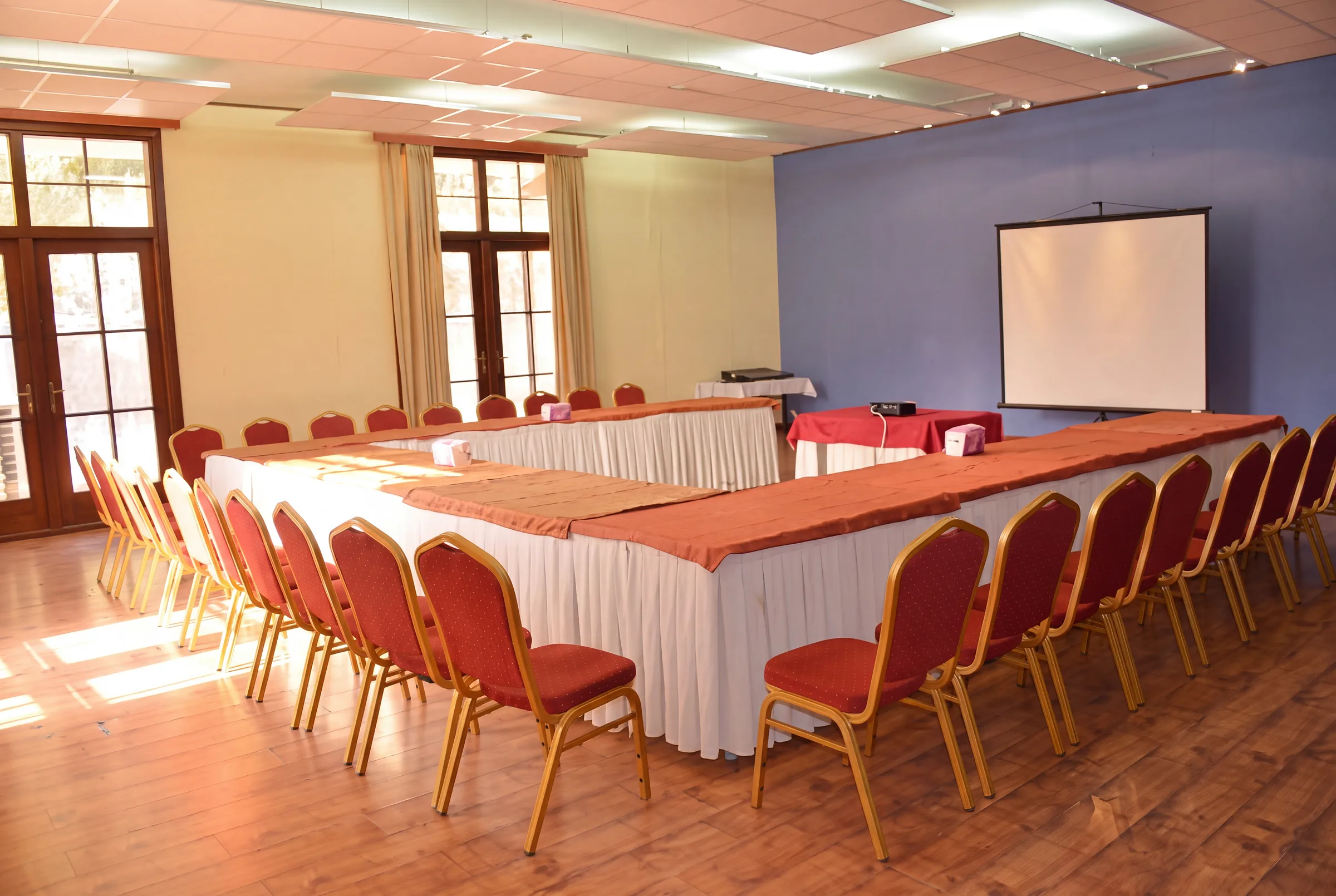 One of our halls, with a projector screen and daylight through tall windows.