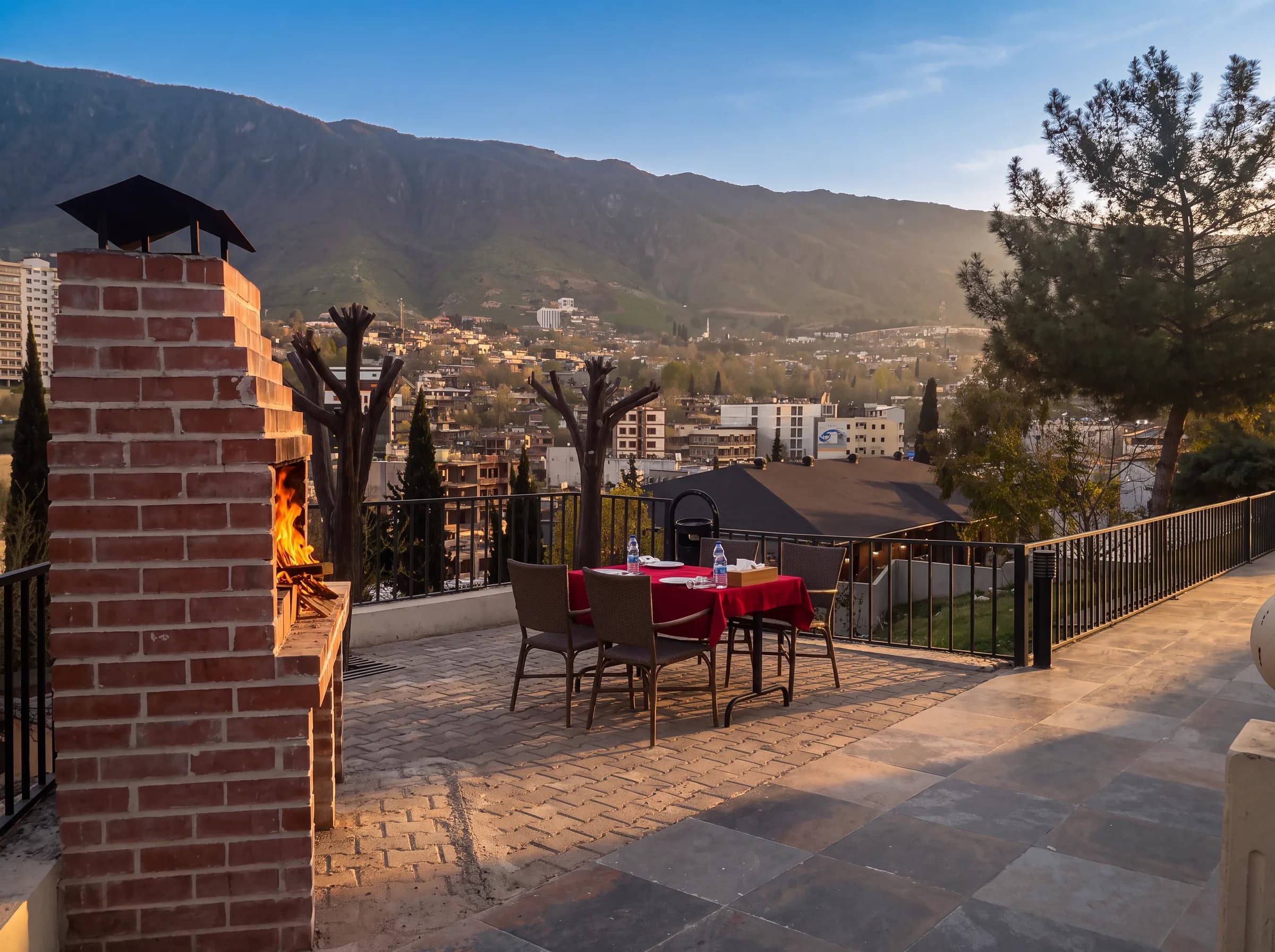 A terrace with a lit barbecue and a set table, looking over Shaqlawa to Safeen Mountain